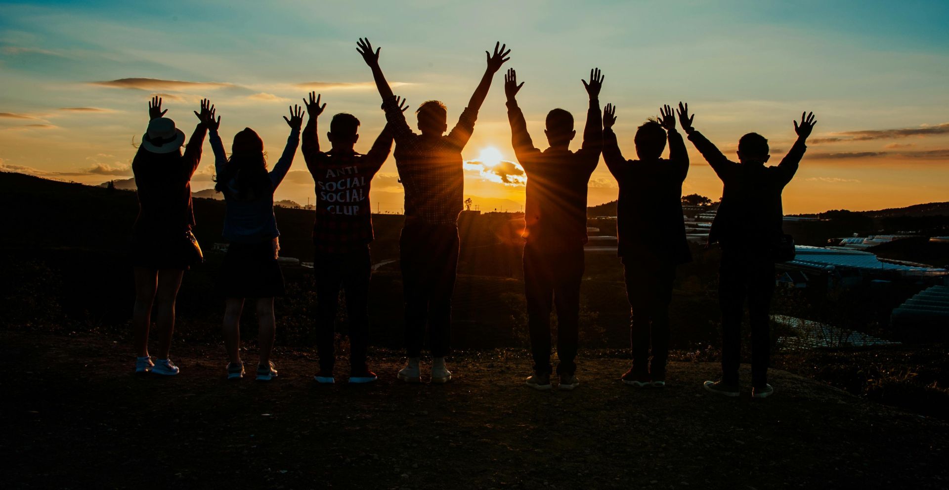 A diverse group of friends raises their arms in celebration against a vibrant sunset backdrop.
